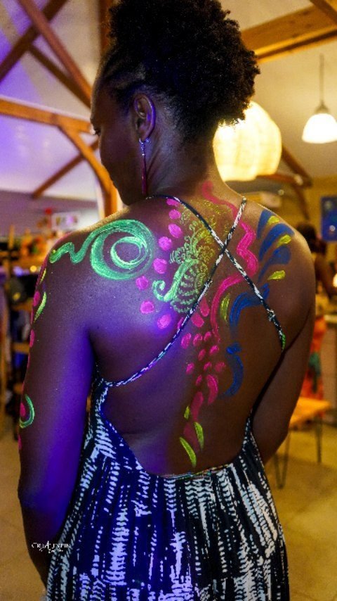 Dos d'une femme peint de motifs fluo qui s'illuminent sous la lumière noire, atelier Artpluriailes